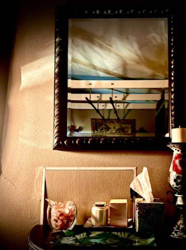 A framed mirror above tissues, folded towels and small room essentials in warm light.