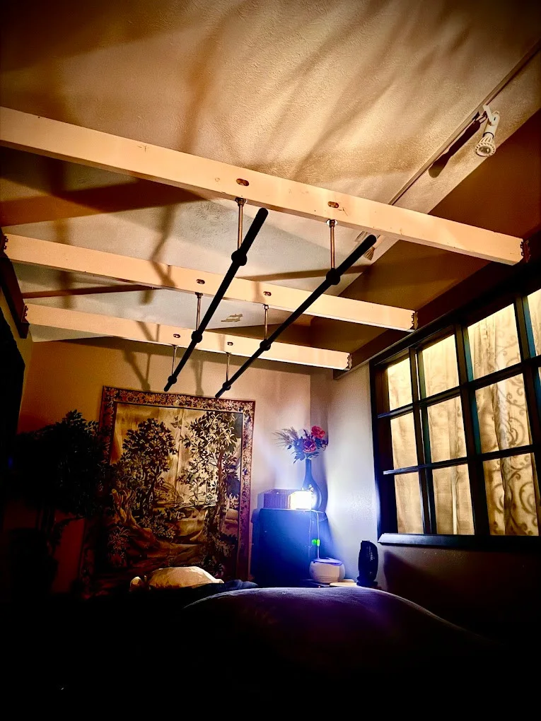 Timber beams, overhead massage bars and a patterned privacy curtain in a dim treatment room.